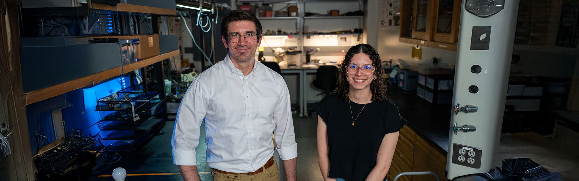 A laboratory scene featuring two individuals under blue lighting, collaborating on experiments and research activities.